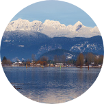 Clouds rolling over mountains in Coquitlam, Canada, with deciduous trees and water sitting at the foot of the mountain.