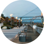 A promenade in New Westminster (Canada), with benches all the way along and a large steel bridge in the background.