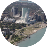 A scene of Windsor in Canada. City with skyscrapers, buildings and trees sitting in front of water.