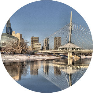 A wintery image with water surrounded by city buildings and a large bridge running over it.