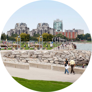 Paved walkway surrounding water in Burlington, with city buildings in the background.