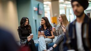 A group of women talking while holding a cup of coffee.