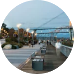 A promenade in New Westminster (Canada), with benches all the way along and a large steel bridge in the background.