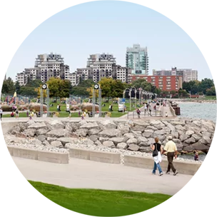 Paved walkway surrounding water in Burlington, with city buildings in the background.